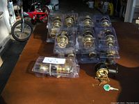 Seven brass-finish door passage locks displayed in plastic trays on a table in a garage, with a Schlage deadbolt lock with keys separated outside the packaging.
