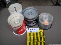 Photo of three spindles of blank discs including Comstock CD-R and DVD+R discs with yellow boxes of calculator paper rolls in front reviewed for lot contents.