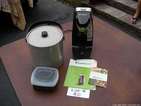 Overall view of Foodsaver bag sealer unit, metal ice bucket with lid, Joie ice cube tray with lid, and owner's manual on table.