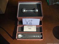 Two shots showing a new in box Lenox pewter baby spoon and baby rattle set in original packaging with foam inserts and brand card.