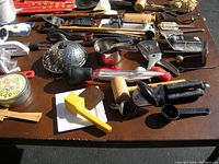 Overview of various kitchen utensils and tools laid out on a table including graters, rolling pin, mallet, scoopers, garlic press, and other items.