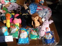 Overhead image showing several TY Beanie Babies still in original Happy Meal packaging with other assorted stuffed animals including an American flag elephant and small brown stuffed monkey.