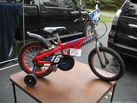 Full side view showing the red Schwinn Cosmo 16 inch kids bike with training wheels on a stand outdoors.