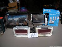 Wide shot of entire lot showing all items on table; 2 Timex alarm clocks, Discovery Kids light with safari animals, AT&T cordless phone box, magnifying shield on stand, and an aquarium or display with safari animals.