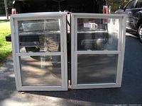 Photo showing both vinyl replacement windows side by side outdoors, with visible screens and sliding panes.