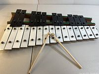 Full 25-key metal xylophone with wooden base, black and white keys labeled with musical notes. Two wooden mallets placed crossed on the instrument.
