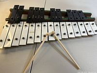 Front view of xylophone showing natural white keys labeled with notes and black sharp/flat keys, with mallets crossed on top.