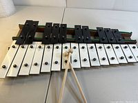 Front view of metal keyed xylophone with wooden base, showing 25 keys arranged chromatically, black and white keys, with two sticks placed on top.