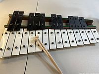 Photo showing the 25 keys metal xylophone with white and black keyed notes arranged on a wooden base. Includes two wooden mallet sticks placed on the keys.