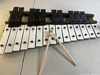Front view of 25-key metal xylophone with black and white keys labeled with musical notes and a pair of wooden mallets resting on the keyboard.