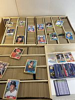 Cardboard box containing multiple rows of 1987 Topps baseball cards with gold borders, several loose cards laid across compartments