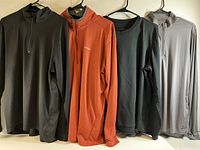 Four men's XL long sleeve quarter-zip pullover shirts hanging on hangers showing color and brands