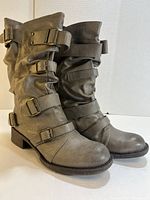 Left-front angled view of the gray leather boots showing detail of slouchy texture and multiple buckle straps.