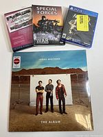 Photo showing all three items: Jonas Brothers vinyl LP, Special Forces DVD, Fallout 76 PS4 game, all shrink wrapped