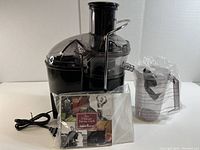 Front view of the Jack LaLanne Fusion Juicer with instruction booklet and measuring cup wrapped in plastic.