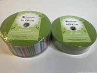Two rolls of Member's Mark premium wired edge ribbon, one 2.5 inches wide by 50 yards long with assorted designs, and one 1.5 inches wide by 50 yards long with solid green color.