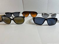 Overview of five pairs of men's sunglasses with varied frame and lens styles arranged with two in front and three behind.
