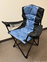 Blue and black oversized camping chair with padded seat, backrest, and armrests, displayed unfolded on floor showing heavy duty metal frame and fabric details.