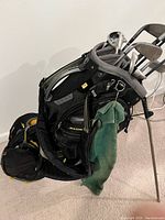 Side angle of Nike SasQuatch black golf bag showing padded straps, several zip pockets, and golf clubs inside pocket openings