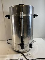 Front view of Regalware coffee maker showing spigot, water level gauge, power switch, and black plastic handles