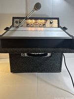 Front view of the lecternette showing microphone mounted on a flexible arm, control panel with multiple switches, and illuminated indicator light.