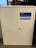 Front view of a white metal cabinet labeled 'Sellstrom Monitor The Ultimate Germicidal Cabinet' with lock and keyhole visible.