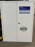 Full view of the white metal cabinet with Sellstrom Monitor label showing goggles graphics and AOS Academy of Science sticker.
