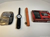 Four measuring devices arranged on a table: boxed Maverick Remote Cooking Thermometer, black Acurite dial thermometer, Berg & Sons hydrometer in pink-orange tube, and Taylor Connoisseur thermometer in secure packaging.