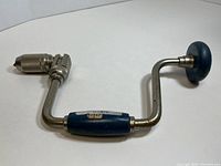 Full side view of a vintage 12-inch bit brace with blue permaloid grip and knob, metal frame and chuck.