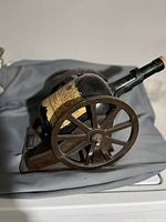Side view of antique-style metal cannon holding large Cognac bottle horizontally