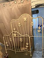 Full view of solid metal headboard and footboard, showing their cream color, curved bars, and floral and butterfly metal designs.