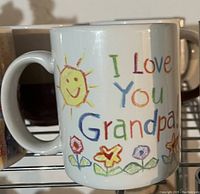 Front side of the mug with colorful child-like drawing and text 'I Love You Grandpa!' with sun and flowers.
