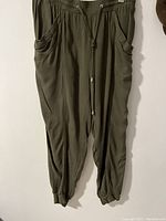 Front view of olive green khaki pants showing elastic waistband with drawstring, side pockets, and elastic cuffs at ankles