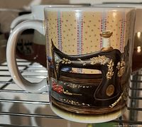 Photo of a white ceramic mug featuring a detailed illustration of a vintage sewing machine with gold floral designs, with patterned wallpaper background and pin cushion detail.