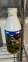 One white opaque milk glass bottle with a colorful farm-themed graphic including a farmhouse, animals, and blue sky