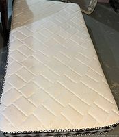 Top view of twin mattress showing white quilted fabric with stitched diamond pattern