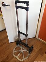 Two wheel fold-up dolly unfolded and standing upright showing metal base plate and extendable handle with two foam grips.