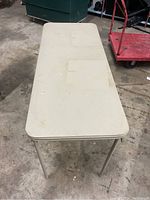 Top view of the rectangular folding table showing cream/off-white tabletop surface with rounded corners and some wear marks.