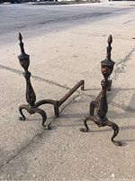 Pair of antique metal andirons displayed on pavement showing overall form and size.