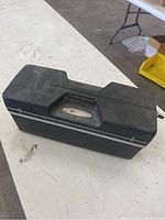 Closed black plastic Sears branded tacklebox with top handle on a white table.