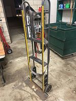 Full view of the appliance dolly standing upright showing yellow metal frame, black securing straps, and two wheels.