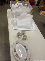 Photo showing three small coffee cups with holly leaf and berry design and a large oval plate with floral and gold trim design on a white surface.