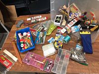 Top view of a cluttered table covered with fishing tackle including floats, lures, line spools, plastic containers, ropes, and packaging.