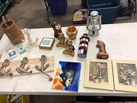 Full view of all items on table including nautical anchors, lantern, lighthouse suncatcher, wooden horse head, animal figurine, basket, tile, cross, and framed floral prints