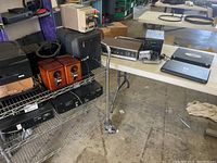 Photo showing a table and rack with various electronic items including speakers, a microwave oven, cassette player and other boxes and cables.