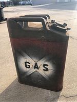 Photo showing front side of a metal military gas canister with 'GAS' stenciled on a white faded background over a red band, handle on top, cap with chain.