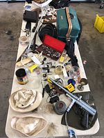 Wide view of table with green tackle box, paintball gun, hats, cords, collectibles and tools