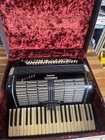 Accordion in open case showing red plush interior and piano keyboard