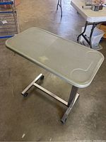 Full view of rolling medical food tray with rectangular grey plastic top and metal base on wheels.
