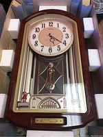 Seiko wall clock in original packaging showing full clock face and pendulum design.